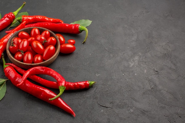 Vista superior de pimientos rojos picantes y hojas de laurel y un tazón de tomates cherry en el lado izquierdo de la mesa negra con espacio de copia