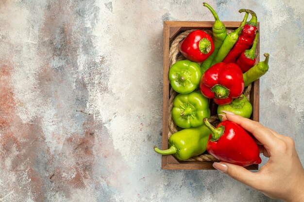 Vista superior pimientos rojos y verdes pimientos picantes en caja de madera pimiento en mano de mujer en lugar de copia de superficie desnuda