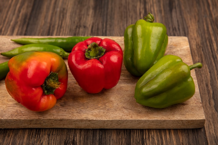 Foto gratuito vista superior de pimientos rojos y verdes en una tabla de cocina de madera sobre un fondo de madera