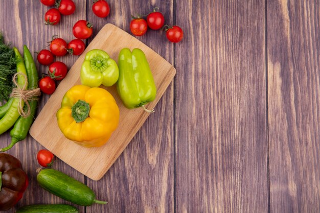 Vista superior de pimientos en tabla de cortar con eneldo tomates y pepinos en superficie de madera