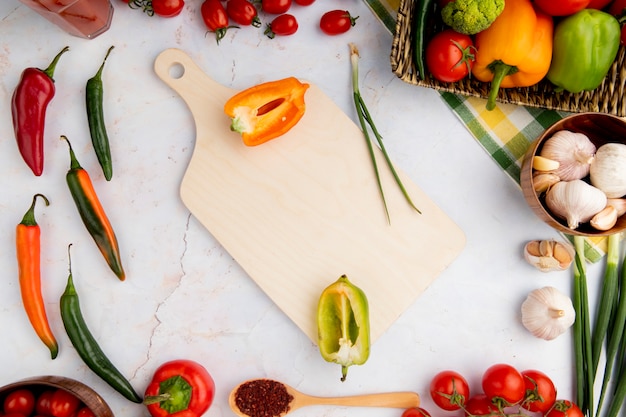 Vista superior de pimientos con tabla de cortar y otras verduras sobre superficie blanca