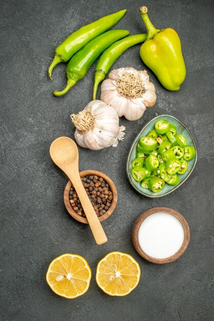 Vista superior de pimientos verdes picantes con limón y ajos sobre un fondo oscuro