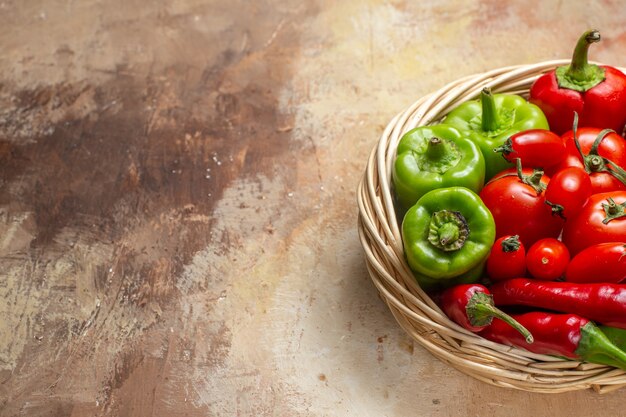 Vista superior de pimientos verdes y rojos pimientos picantes tomates en canasta de mimbre sobre fondo ámbar