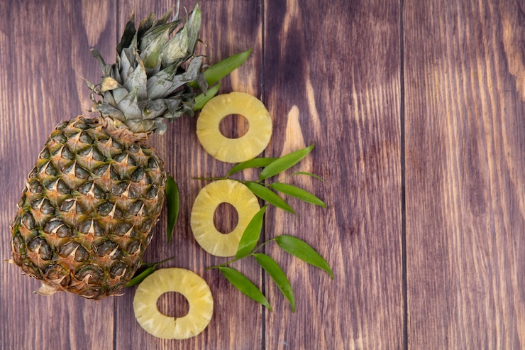 Foto gratuito vista superior de piña con rodajas de piña y hojas sobre superficie de madera