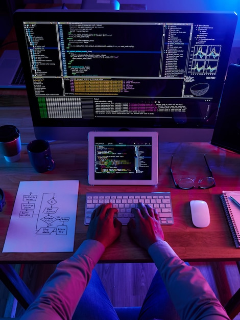 Vista superior del pirata informático irreconocible que realiza un ciberataque por la noche