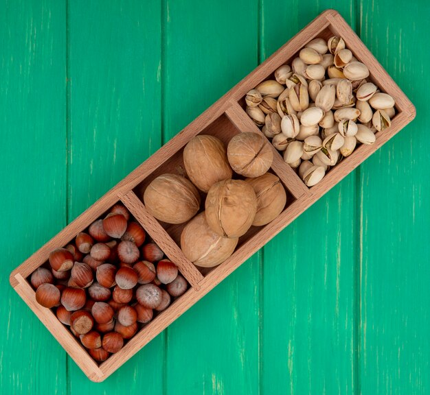 Vista superior de pistachos con avellanas y nueces sobre un soporte de madera sobre una superficie verde