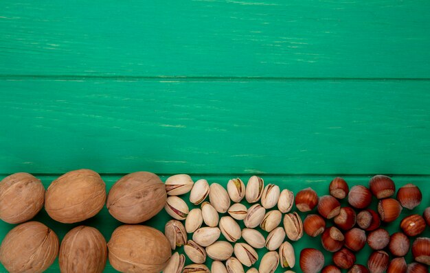 Vista superior de pistachos con avellanas y nueces sobre una superficie verde