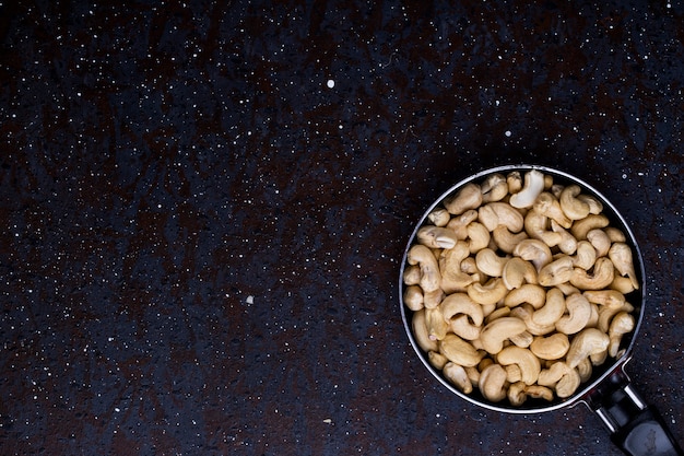 Vista superior de pistachos tostados salados en una sartén sobre fondo negro con espacio de copia