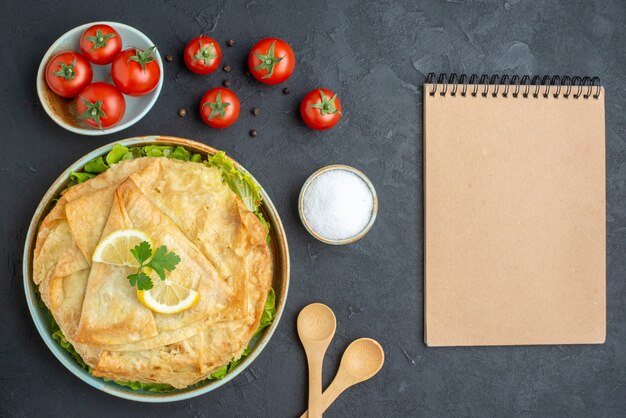 Vista superior de pita cocida dentro de la placa con verduras de limón y tomates sobre una superficie oscura