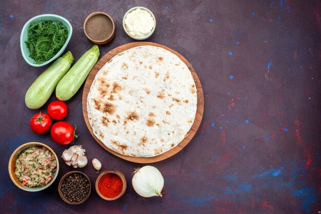 Vista superior de pita redonda con verduras frescas y condimentos en superficie oscura