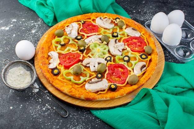 Vista superior de la pizza de champiñones con tomates, aceitunas, champiñones, todos en rodajas por dentro con harina en el escritorio gris, masa de pizza de tejido verde italiano