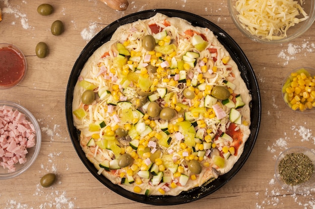Vista superior pizza cruda en sartén con ingredientes