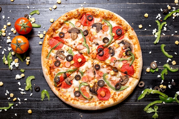 Vista superior de pizza de pepperoni con salchichas de champiñones pimiento verde oliva y maíz en madera negra