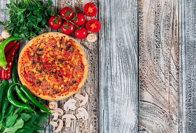 Vista superior pizza con pimientos, champiñones, tomates y grenery sobre fondo de estuco claro. vertical