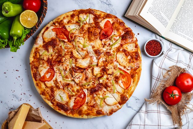 Vista superior de pizza con pollo, ají verde, tomates y queso sobre la mesa