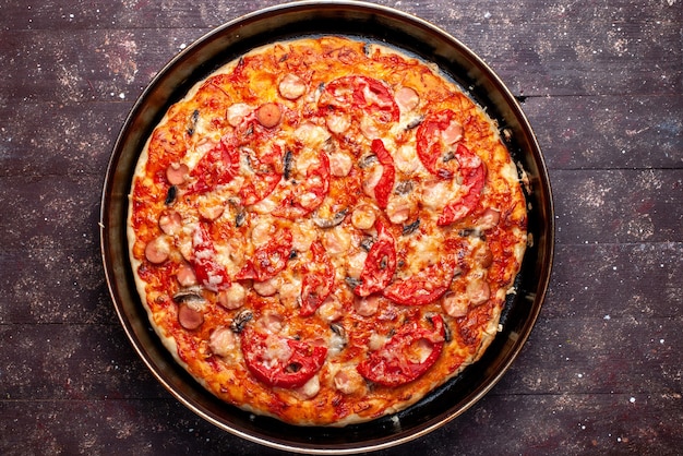 Vista superior de la pizza de tomate con queso con aceitunas y salchichas dentro de la cacerola en el escritorio marrón, comida de pizza comida rápida salchicha de queso