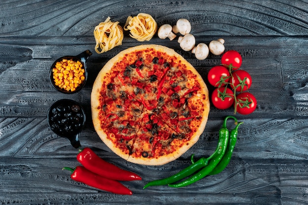 Vista superior pizza con tomates, espaguetis, pimientos, aceitunas, champiñones y maíz sobre fondo de madera oscura. horizontal