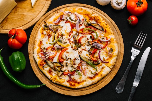 Vista superior de pizza vegetariana con berenjena, pimiento, cebolla roja, tomate y champiñones