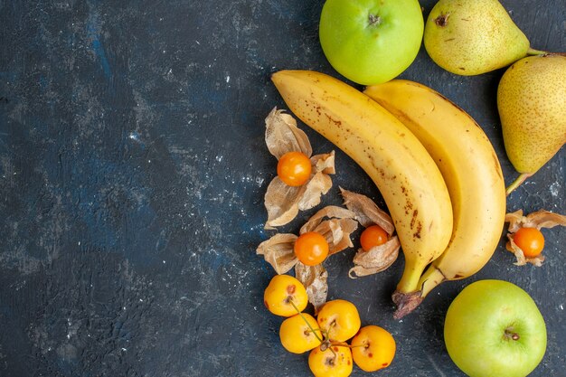 Vista superior de plátanos amarillos par de bayas con manzanas verdes peras sobre el fondo azul oscuro frutas berry vitamina salud fresca