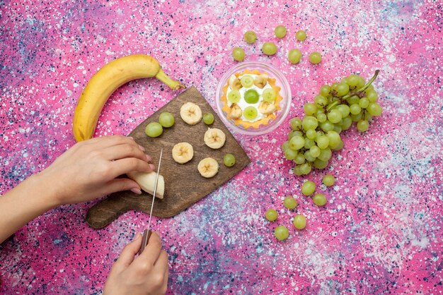 Vista superior de plátanos de corte femenino junto con uvas y pastel en la superficie púrpura dulce de azúcar de fruta