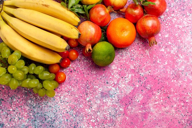 Vista superior de plátanos frescos amarillos deliciosa fruta con uvas y granadas en el escritorio rosa