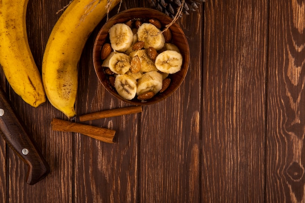 Foto gratuita vista superior de plátanos en rodajas con almendras en un tazón y plátanos maduros frescos con palitos de canela en madera con espacio de copia