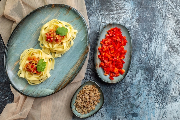 Vista superior de un plato azul con una deliciosa comida de pasta servida con tomate y carne para la cena en una toalla de color canela con sus ingredientes sobre fondo gris