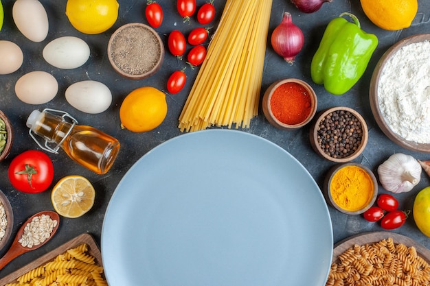 Vista superior plato azul redondo con condimentos de verduras de harina de pasta cruda y huevos sobre fondo oscuro comida masa de huevo cena color de fruta