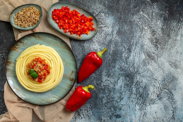 Vista superior de un plato azul con una sabrosa comida de pasta servida con tomate y carne en una toalla de color canela picada y pimientos enteros y cuaderno de espiral
