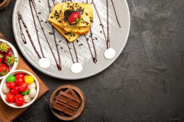 Vista superior del plato de bayas de pastel de chocolate y fresas junto a los cuencos de dulces de chocolate y fresas en la tabla de cortar