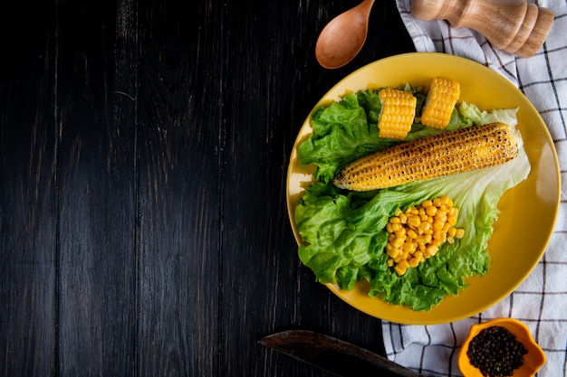 Vista superior del plato de callos enteros y cortados con semillas de maíz y lechuga con cuchillo sobre tela y negro con espacio de copia