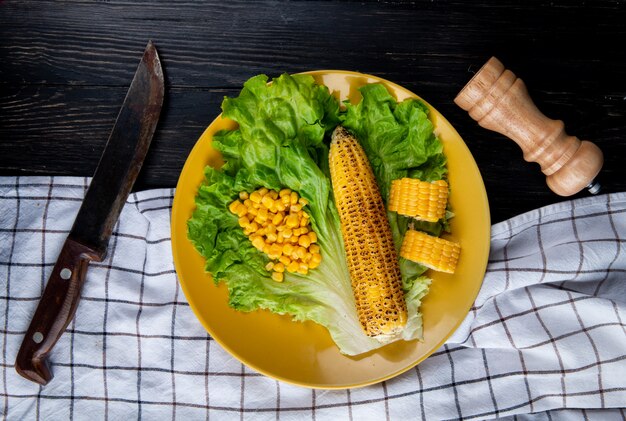 Vista superior del plato de callos enteros y cortados con semillas de maíz y lechuga con cuchillo sobre tela y negro