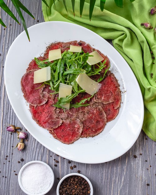 Vista superior plato de carne basturma con rúcula y queso parmesano