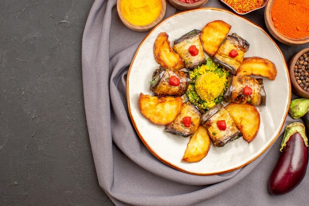 Vista superior del plato cocido de rollos de berenjena con papas al horno y condimentos en negro