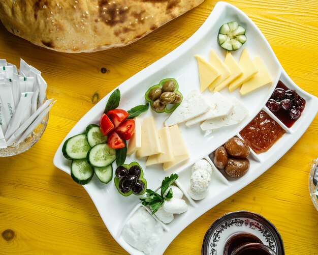 Vista superior de un plato con comida de desayuno con verduras frescas aceitunas queso miel y mermelada servido con té