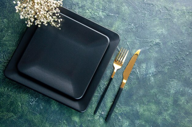 Vista superior plato cuadrado negro con tenedor y cuchillo dorado sobre fondo oscuro cubiertos de comida de color cena cocina restaurante espacio libre