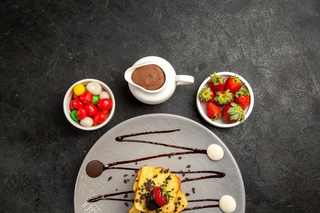 Vista superior del plato de dulces de sabrosos trozos de pastel con salsa de chocolate y fresas junto a los cuencos de dulces fresas y salsa de chocolate