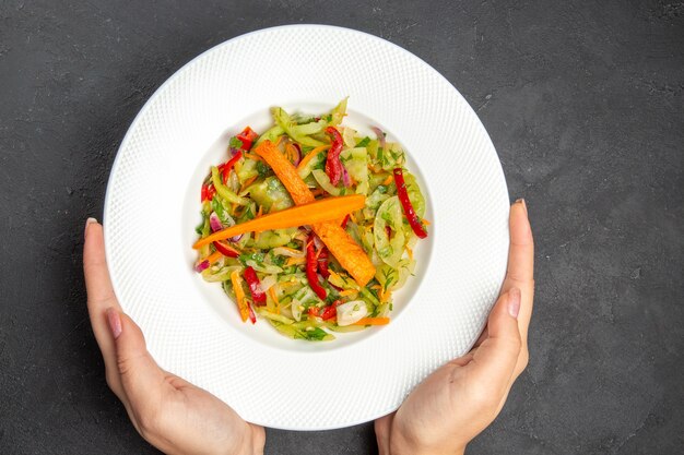 Vista superior del plato de ensalada de una apetitosa ensalada con verduras en las manos