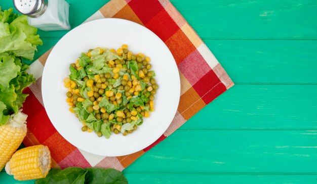 Vista superior del plato de guisantes amarillos y lechuga en rodajas con sal de lechuga de espinacas de maíz sobre tela y verde con espacio de copia