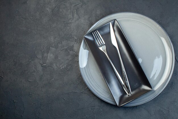 Vista superior plato largo negro con tenedor y cuchillo en plato gris sobre fondo oscuro cubiertos de vidrio colorido feminidad comida de cocina horizontal