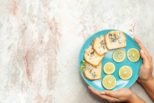 Vista superior del plato de pan y limón de cítricos en rodajas y pan blanco en la mano