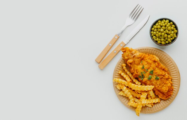 Vista superior del plato de pescado y patatas fritas con guisantes y espacio de copia