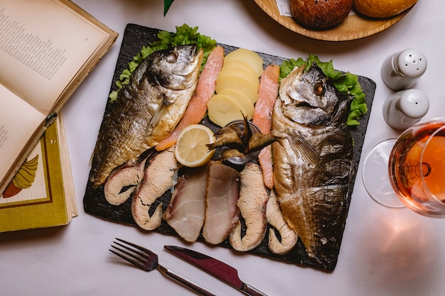 Vista superior plato de pescado con patatas y una rodaja de limón con una copa de vino