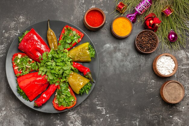 Vista superior del plato de pimientos con hierbas junto a los cuencos de especias coloridas juguetes del árbol de Navidad