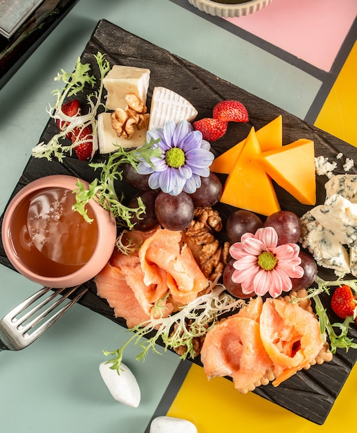Vista superior del plato de queso con salmón ahumado, queso azul, queso cheddar, uva y flores.