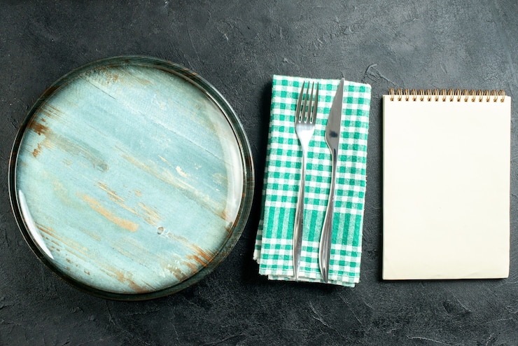 Foto gratuito vista superior plato redondo cuchillo y tenedor en el cuaderno de servilleta a cuadros verde y blanco sobre mesa negra