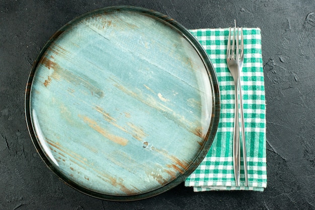 Vista superior plato redondo cuchillo y tenedor en servilleta a cuadros verde y blanco sobre superficie negra