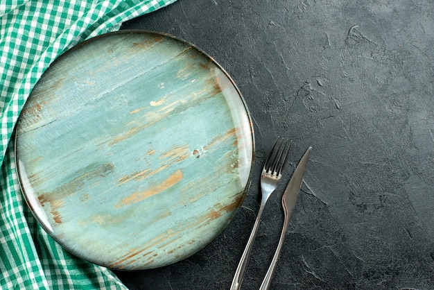 Vista superior plato redondo tenedor y cuchillo mantel verde y blanco sobre mesa negra espacio libre
