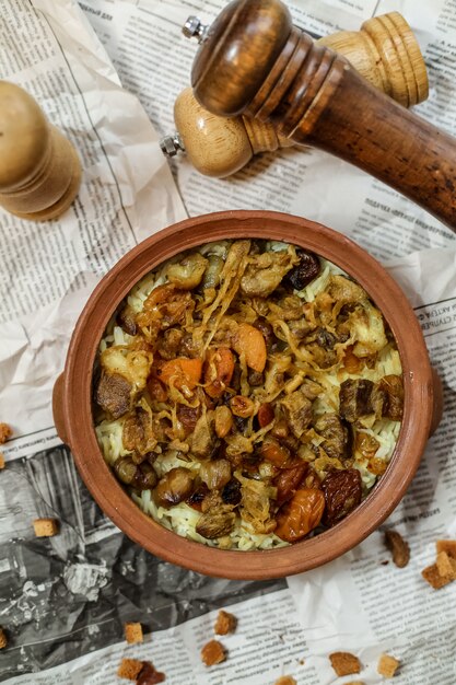 Vista superior de un plato tradicional azerbaiyano pilaf con carne y frutos secos fritos con cebolla en un plato de arcilla en un periódico