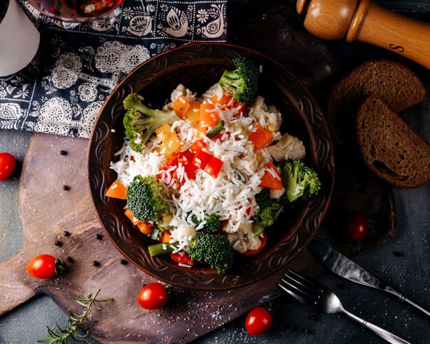 Vista superior plato de verduras incluyendo brócoli tomates rojos y arroz en el piso gris